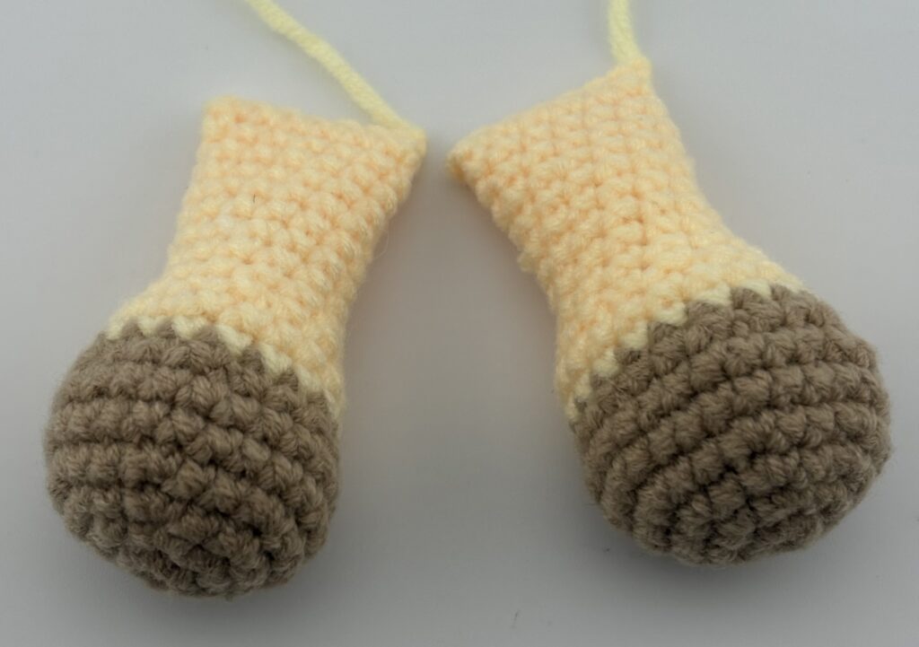 Two amigurumi giraffe legs crocheted with light brown yarn at the paws and light yellow yarn at the arms.