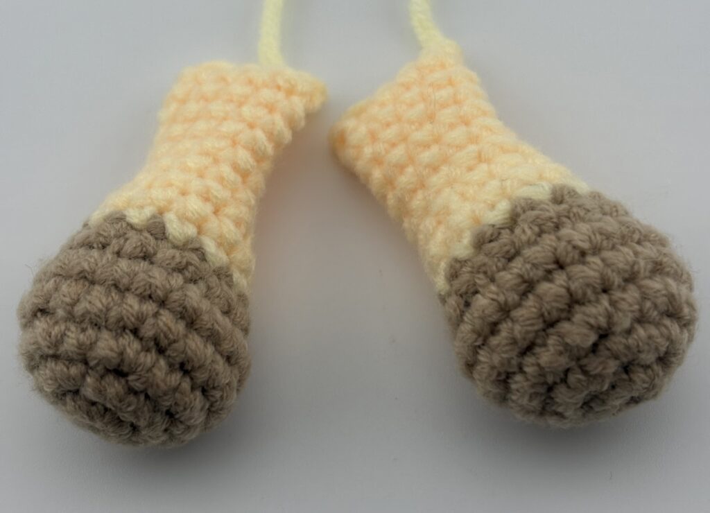 Two amigurumi giraffe arms crocheted with light brown yarn at the paws and light yellow yarn at the arms.