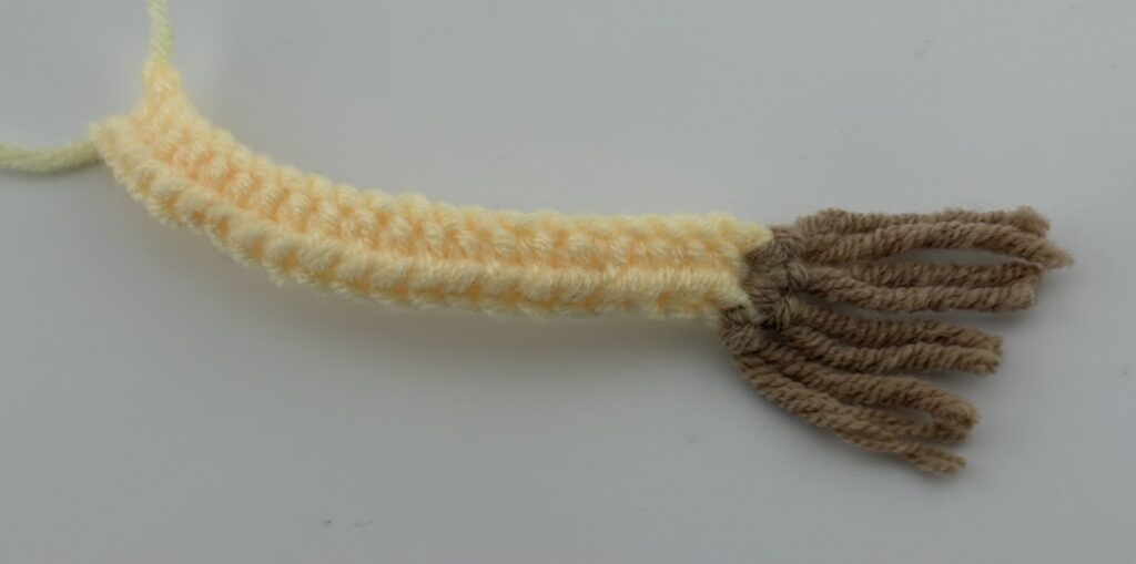 Amigurumi Giraffe tail crocheted with light yellow yarn and brown strands.