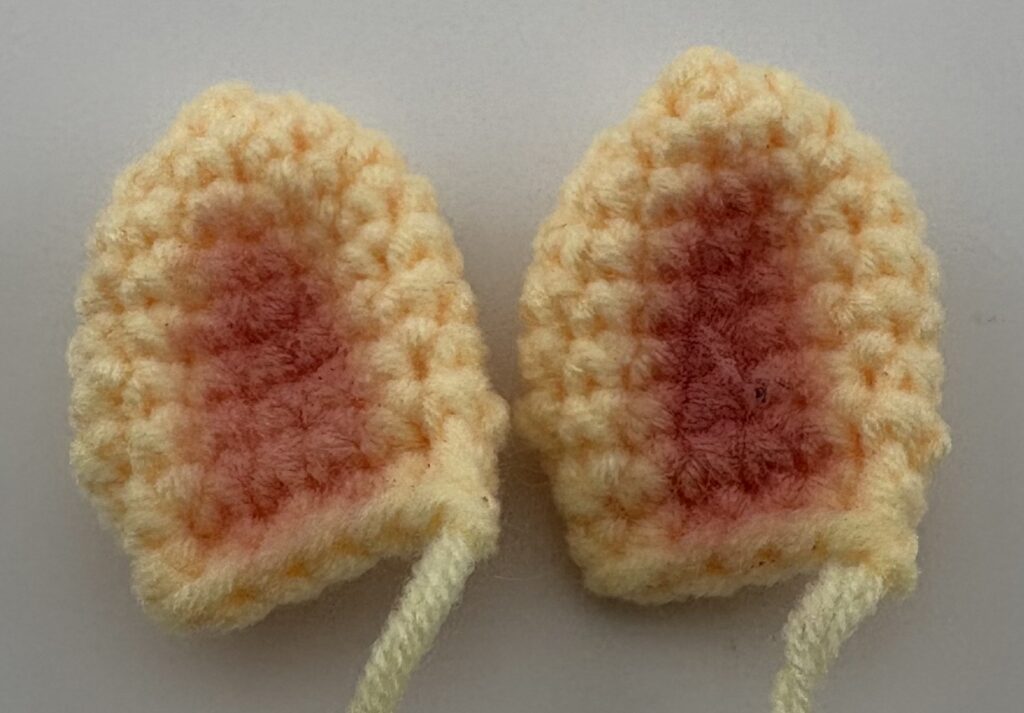 Amigurumi giraffe ears crocheted with light yellow yarn and painted pink on the inside with pink blush.