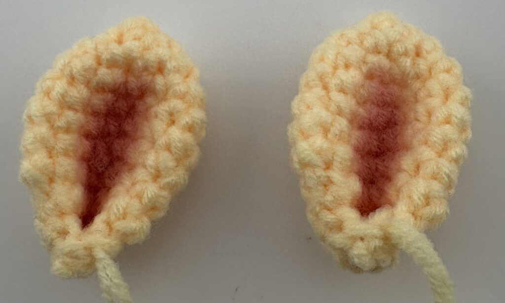 Amigurumi giraffe ears crocheted with light yellow yarn and painted pink on the inside with pink blush.