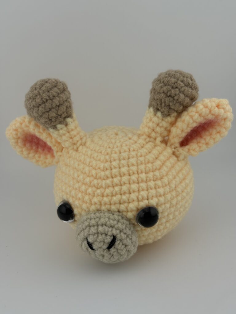 Amigurumi Giraffe head crochete with light yellow yarn, a beige muzzle, two horns and two ears.